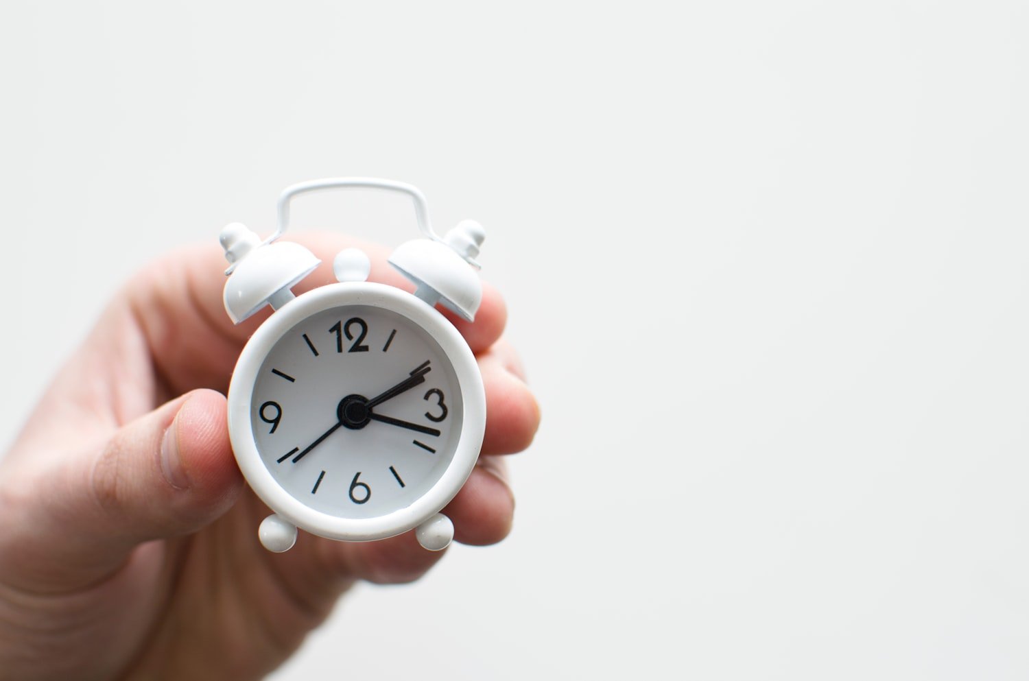 An alarm clock held in a hand, representing the 20-day and 28-day wait-time standards