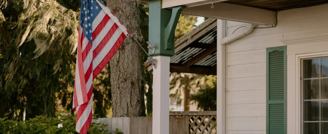 An American flag displayed properly on a white house porch with green shutters
