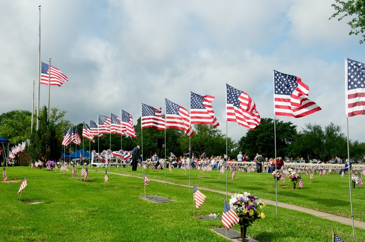 American flags planted across a grass field under a cloudy sky
