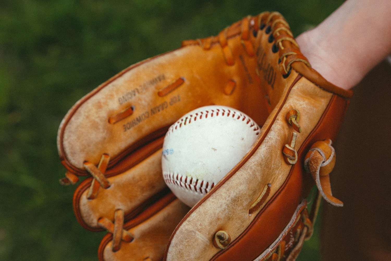 A brown leather baseball mitt with a white baseball resting in it