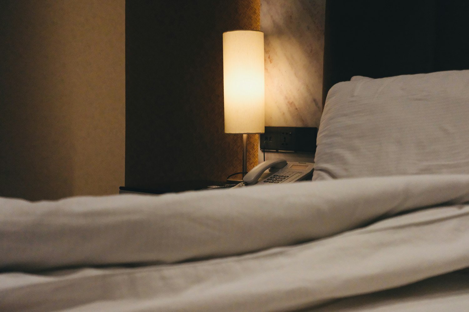A dimly lit bedside lamp and rumpled duvet, representing disrupted sleep secondary to a service-connected condition