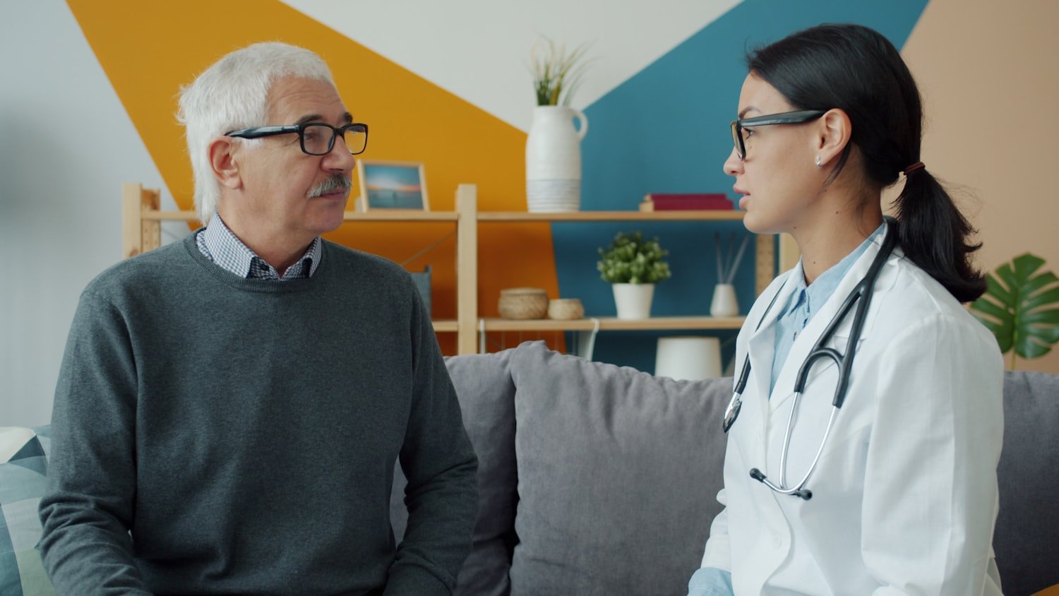 A clinician consulting with an elderly patient on a couch during a home visit