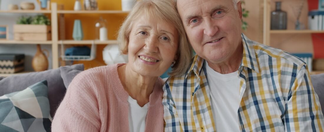 An elderly couple sitting together on a couch at home, the age group VA pension serves