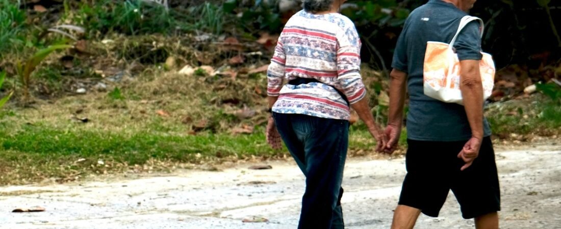 An elderly couple walking hand in hand outdoors, the long horizon a survivor annuity is built for