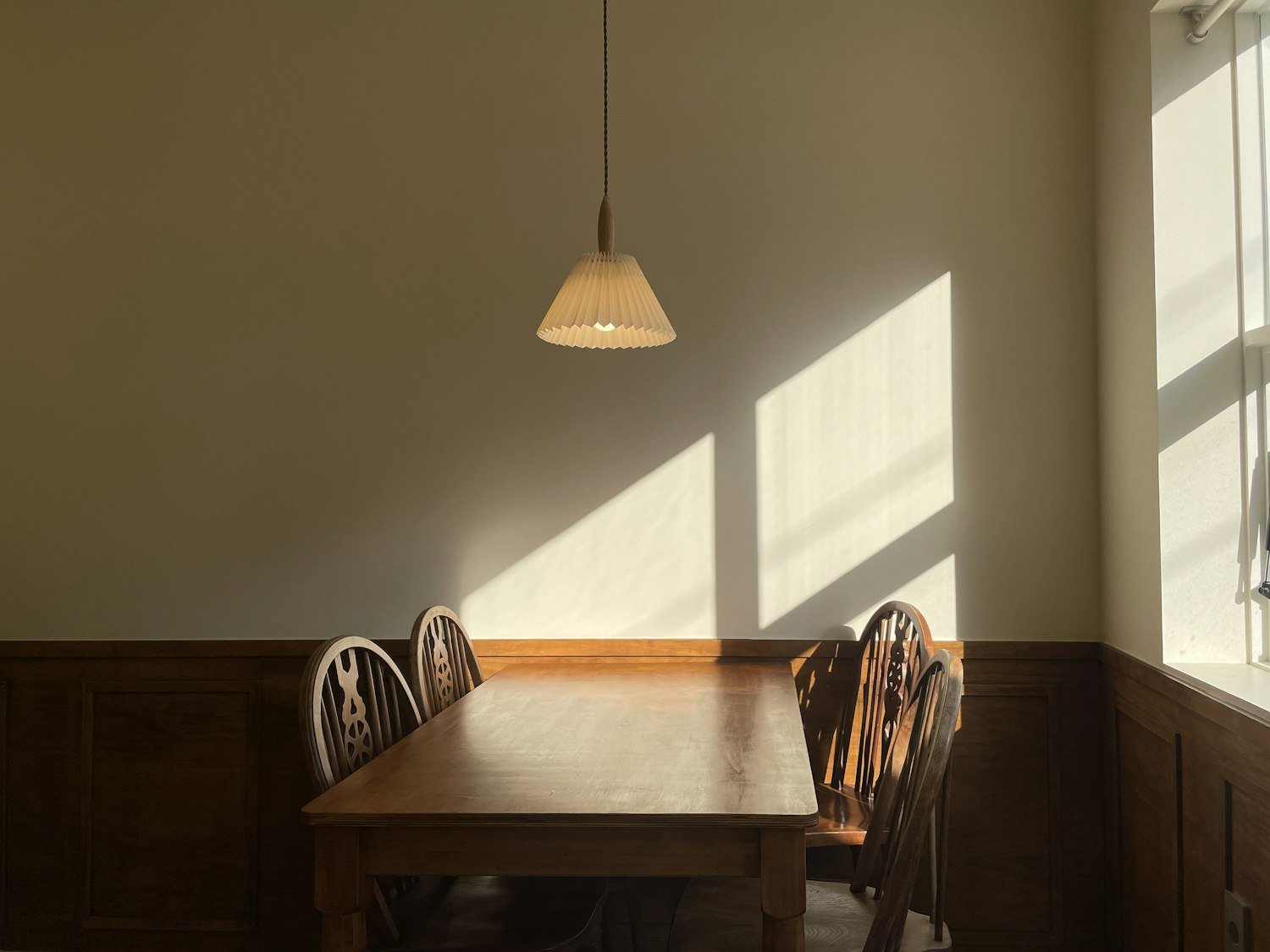 An empty wooden table and chairs in sunlight, evoking a quiet home after a loss