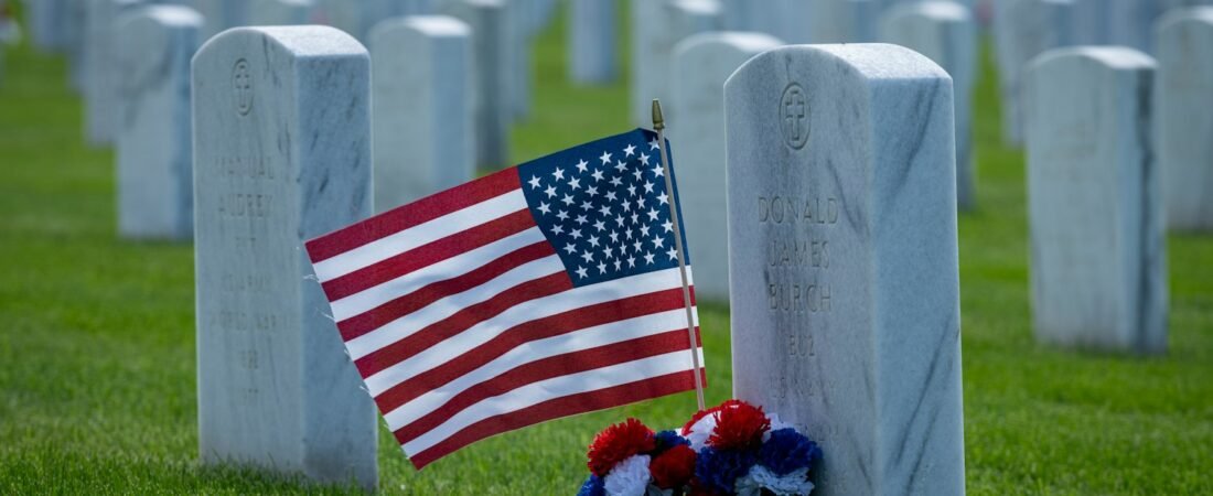 A small American flag and flowers placed at a headstone in a veterans cemetery