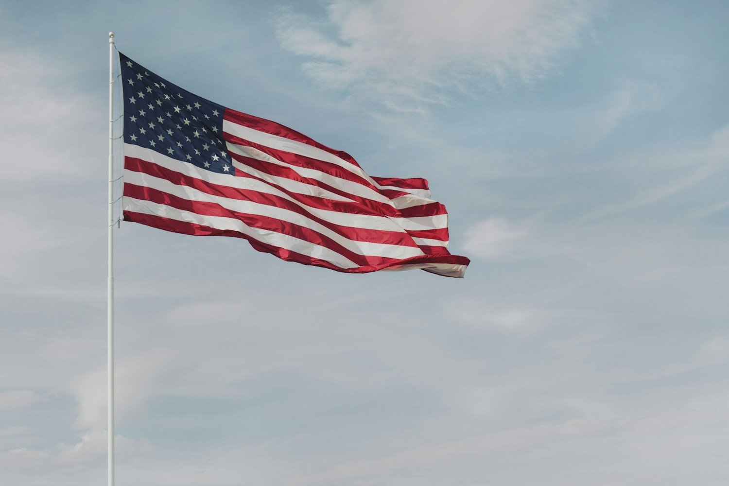 An American flag flying on a pole against a cloudy sky
