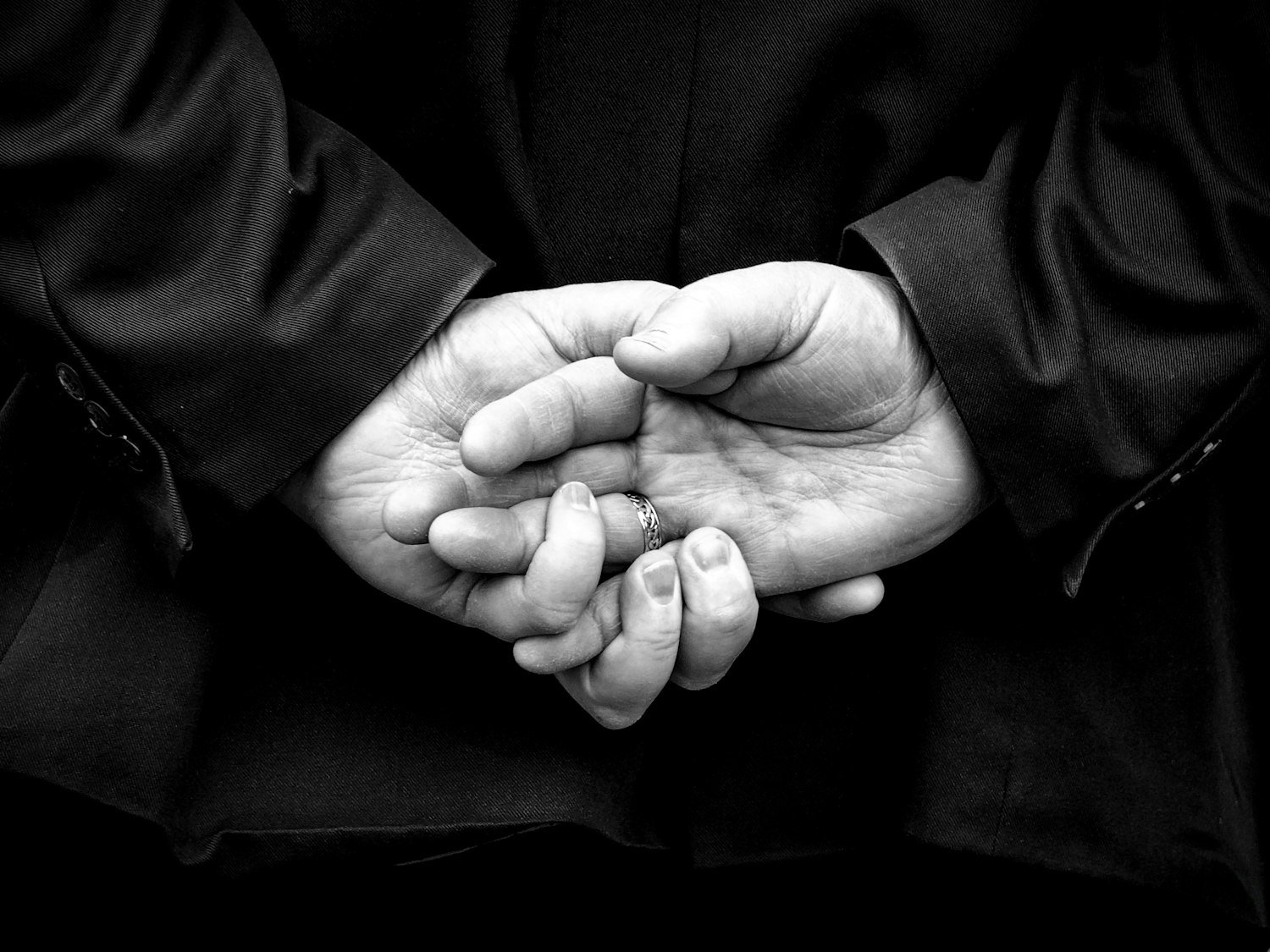 A person standing with hands clasped behind their back in a posture of respect