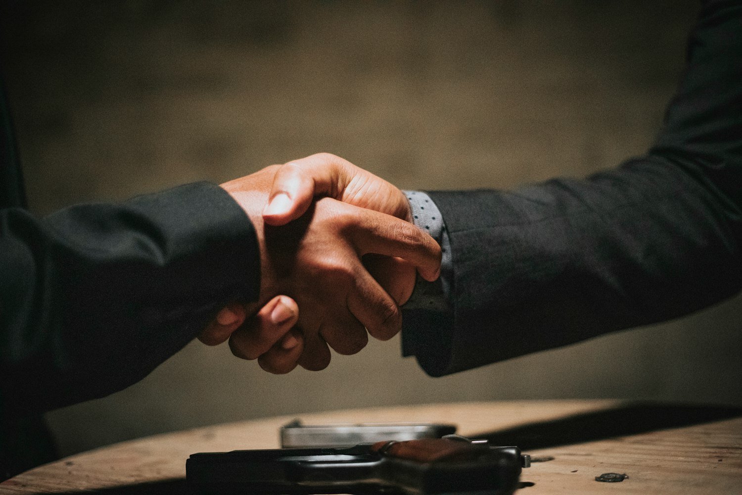 Two people shaking hands over a wooden table after reaching an agreement