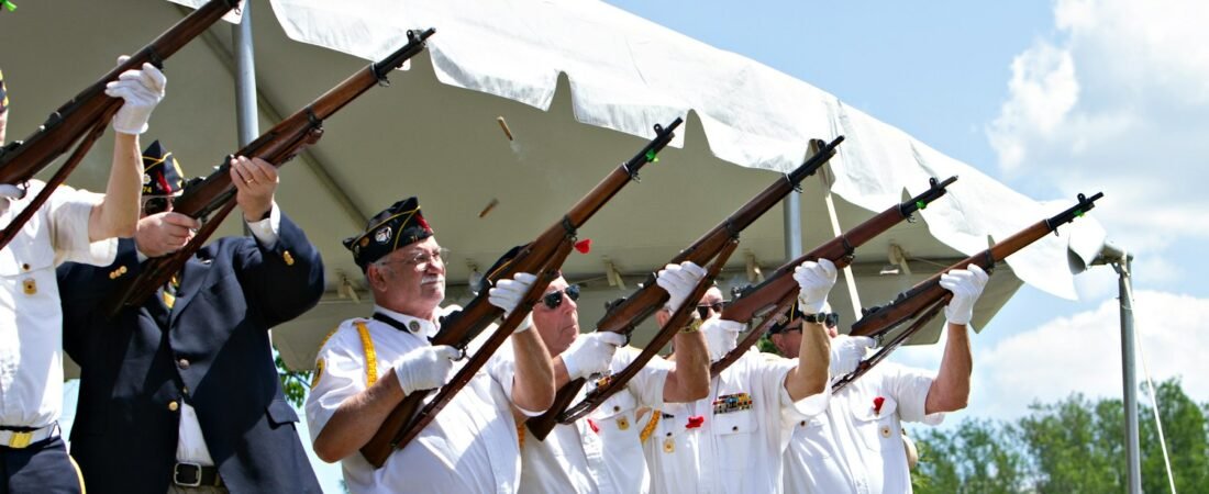 Honor guard members firing a rifle salute during an outdoor military funeral ceremony