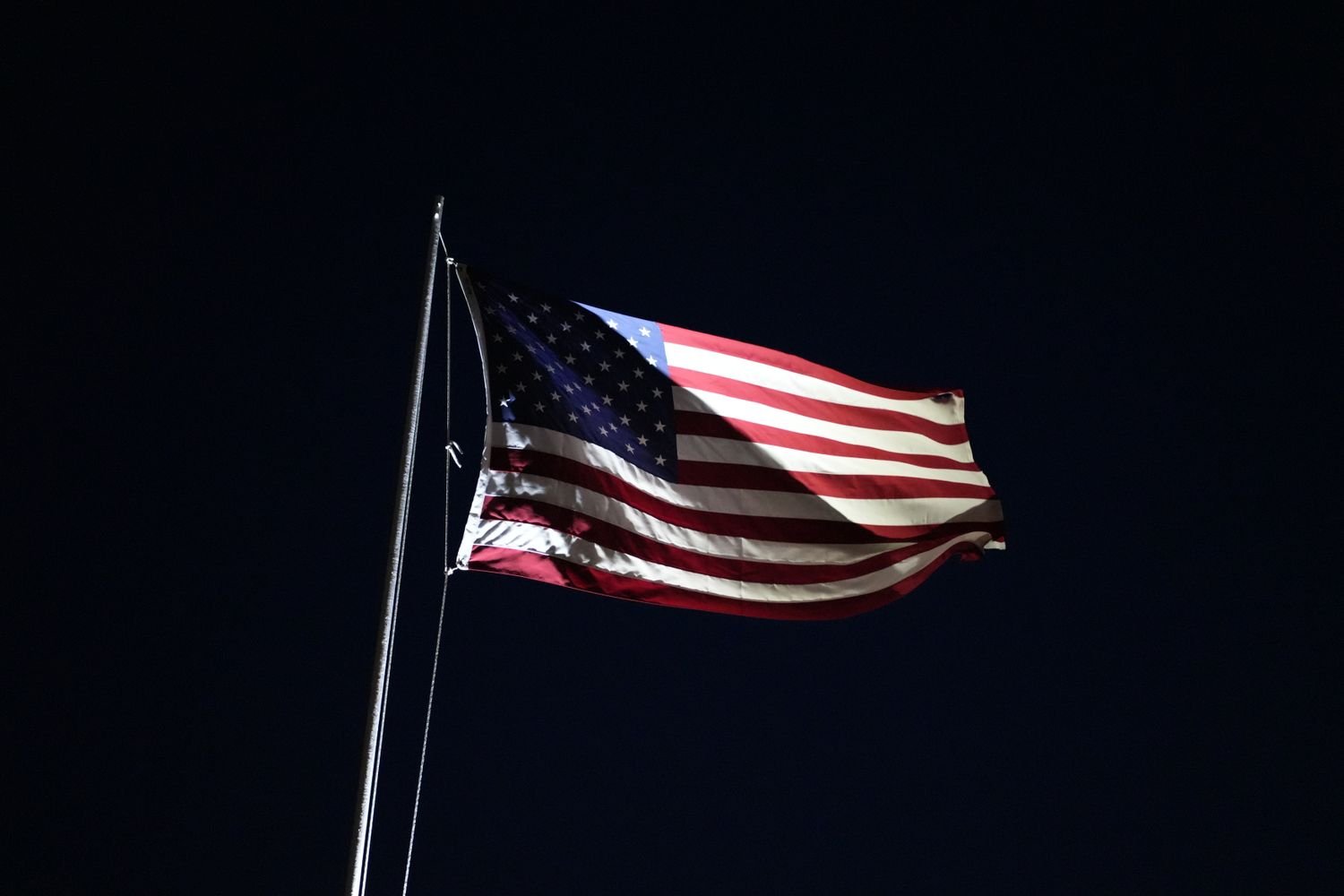 An American flag waving against a dark night sky, which the Flag Code permits when properly illuminated