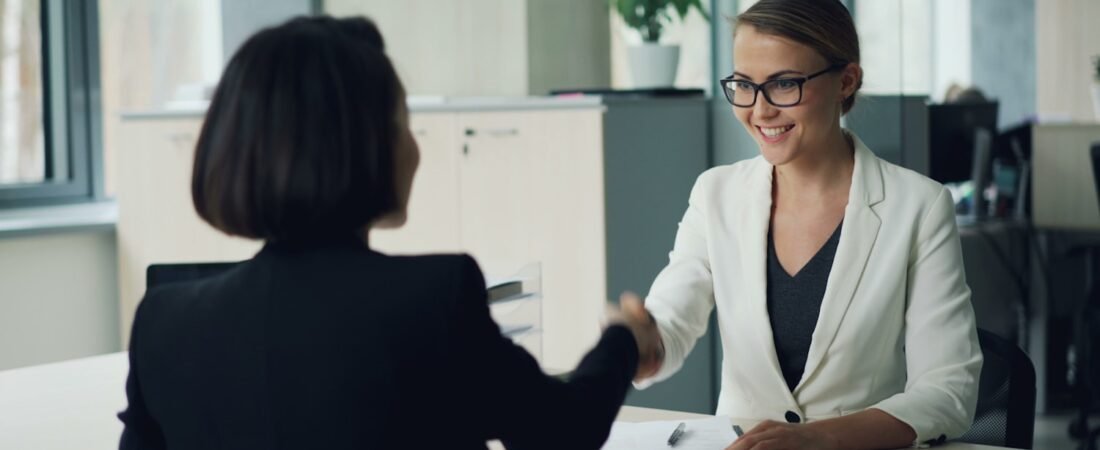 Two people shaking hands across a desk at the end of a job interview
