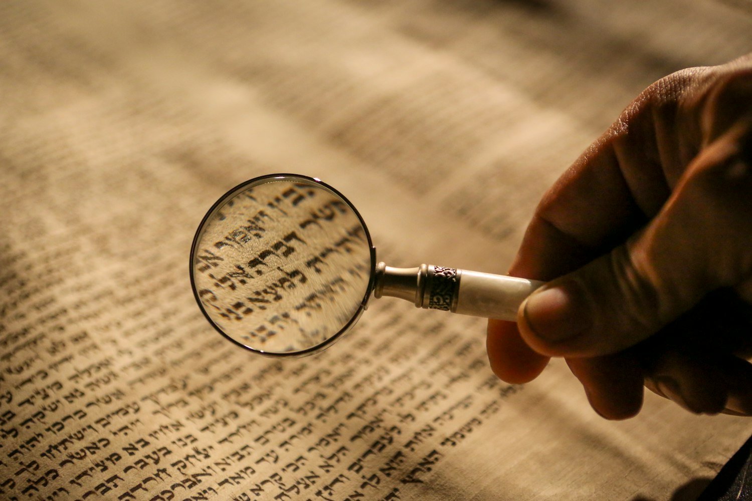 A person holding a magnifying glass over documents while researching records