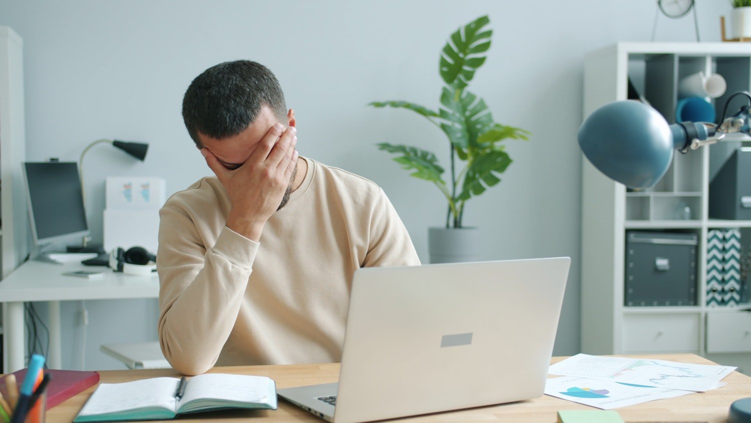 A man rubbing his face in front of a laptop, the workday cost of untreated sleep apnea