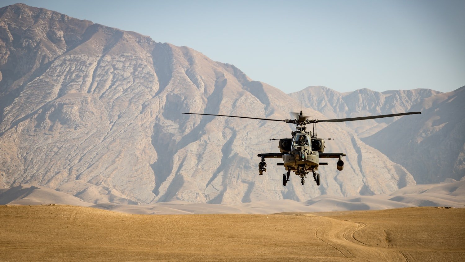 A military helicopter flying over open terrain during a deployment