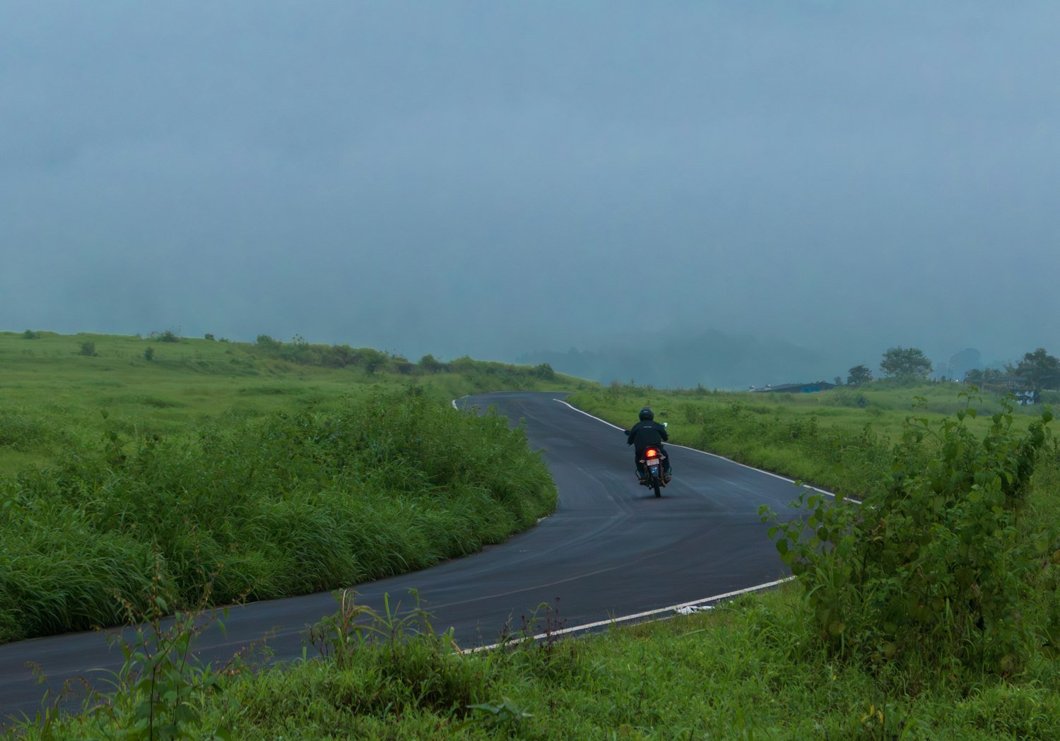 A motorcyclist riding a winding road through grassy hills