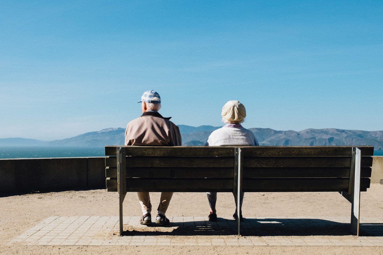 An older couple sitting on a bench together facing the sea