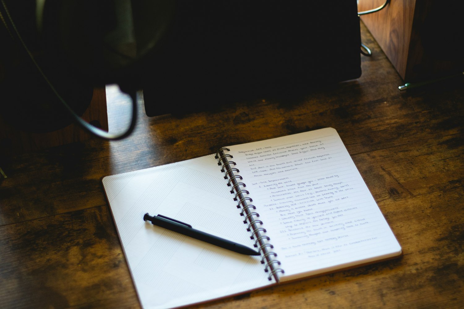 An open notebook with a pen on a desk, for keeping a symptom journal before an exam