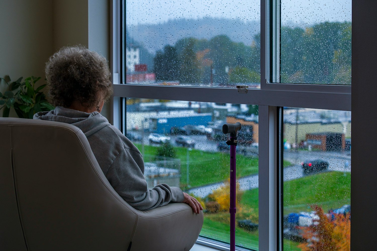 A person sitting in a chair looking out a rainy window, evoking being housebound