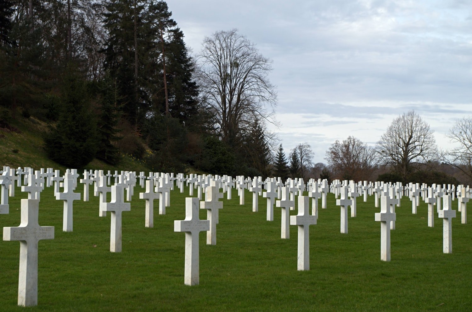 Numerous white cross gravestones in rows on a green cemetery lawn