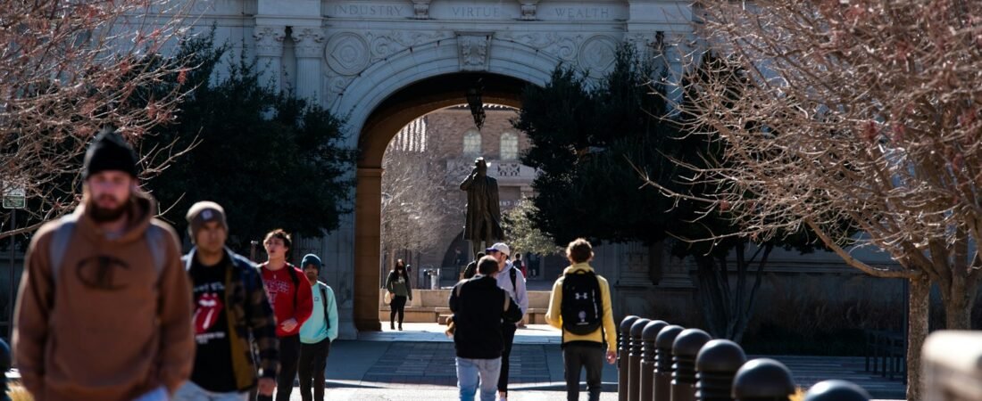 Students walking through a university campus archway, where survivor education benefits are used