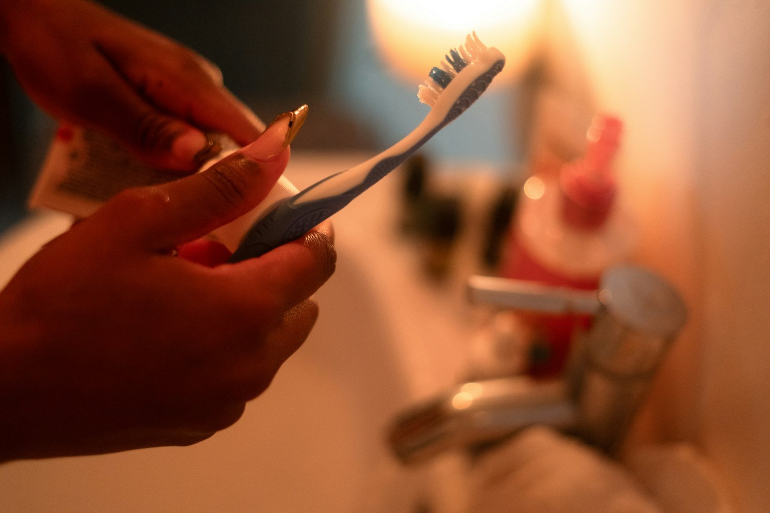 Hands squeezing toothpaste onto a toothbrush, representing routine dental care