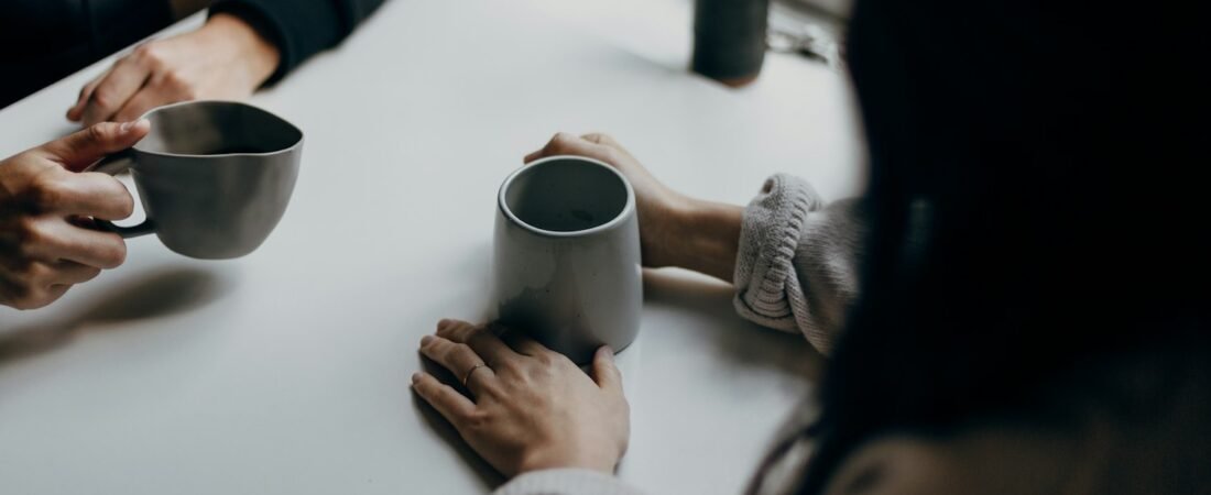 Two people holding mugs across a table, representing a simple check-in conversation with a fellow veteran