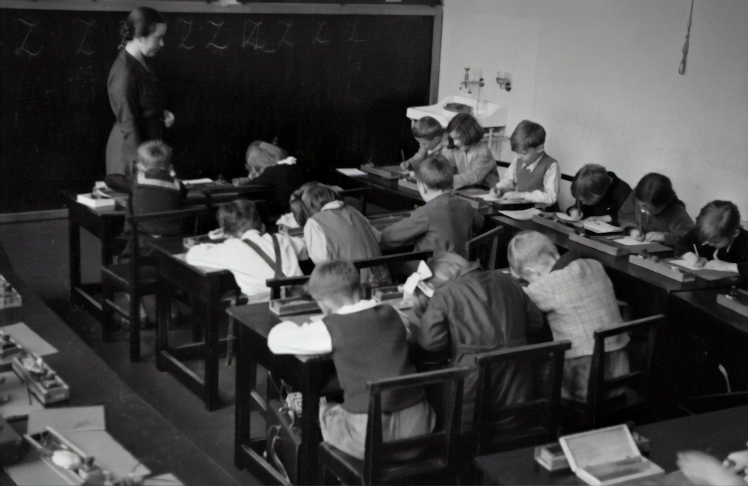 A vintage grayscale photograph of a classroom with a teacher at a chalkboard